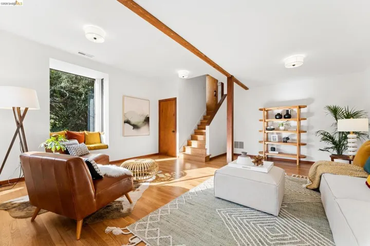 Living area featuring wood-finish flooring, exposed wooden structural beam, built-in window seat, wooden staircase, and flush-mount ceiling lighting