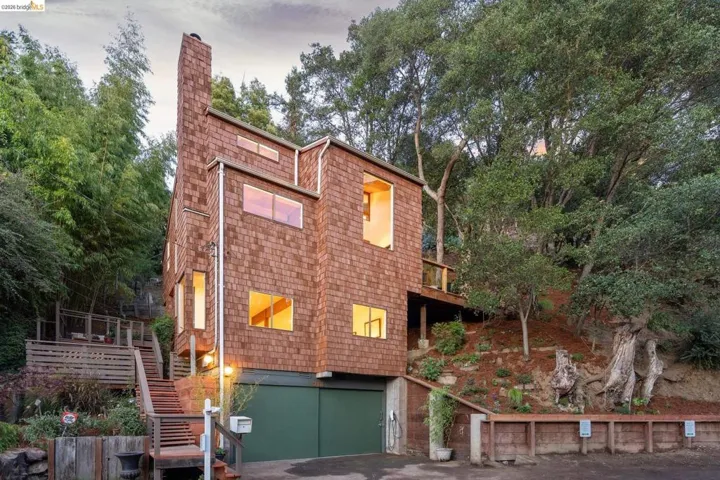 Multi-story residence featuring cedar shingle siding, a prominent chimney, an attached garage, and exterior wood staircases