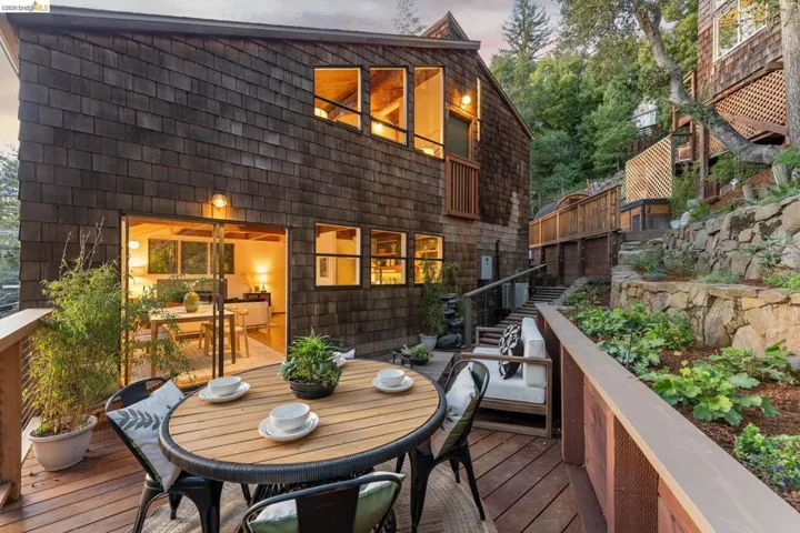 Wood-shingle exterior siding, tiered stone retaining walls, multi-level wood deck, and expansive glass sliding doors