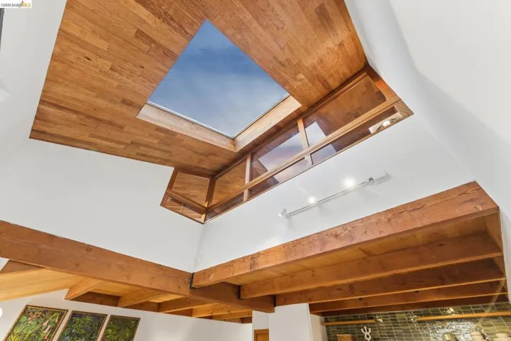 Vaulted ceiling featuring exposed wood beams, wood-paneled ceiling inlay, large skylight, and integrated track lighting