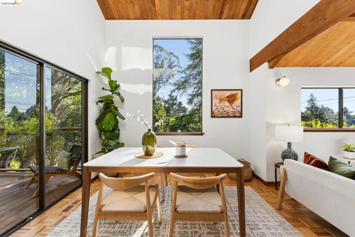 Vaulted ceiling with exposed wood beams, wood-finish parquet flooring, floor-to-ceiling glass sliding doors, and oversized fixed-pane windows