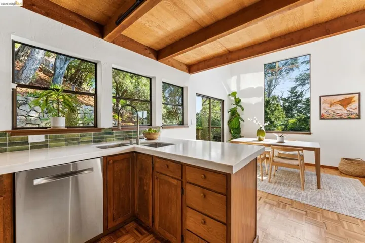 Kitchen featuring wood cabinetry, stone countertops, green tile backsplash, stainless steel dishwasher, and exposed beam ceilings with parquet flooring