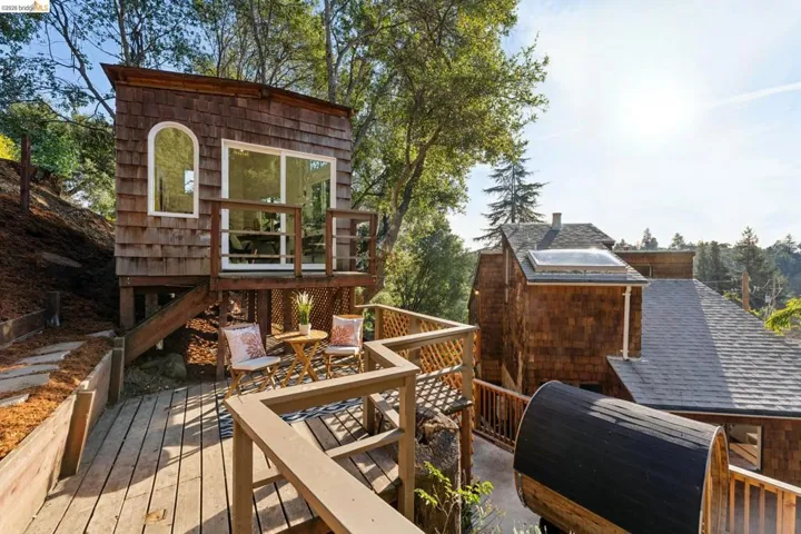 Elevated shingle-sided detached structure featuring wood decking, arched window, sliding glass door, and skylight