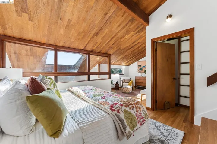 Vaulted wood-plank ceiling featuring exposed beam architecture, extensive horizontal windows with wood framing, built-in wooden door, and wood-finish flooring