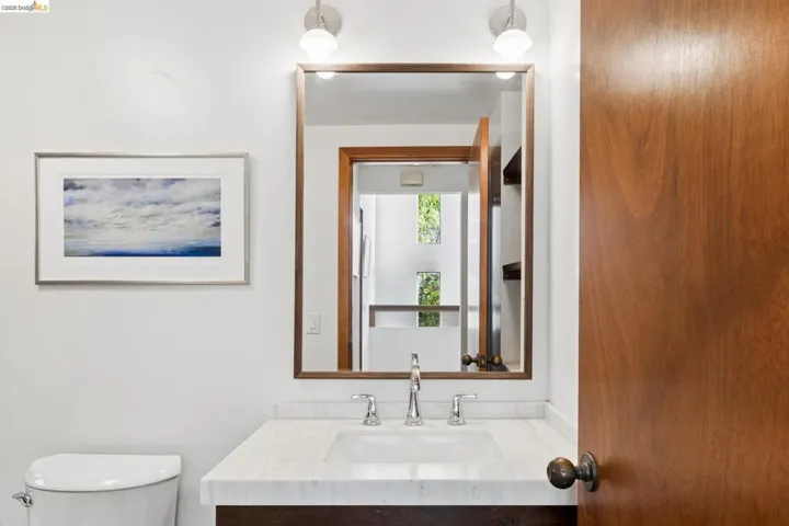 Stone-topped vanity featuring an integrated rectangular sink and polished metal widespread faucet, complemented by a wood-framed rectangular mirror and dual wall-mounted light fixtures