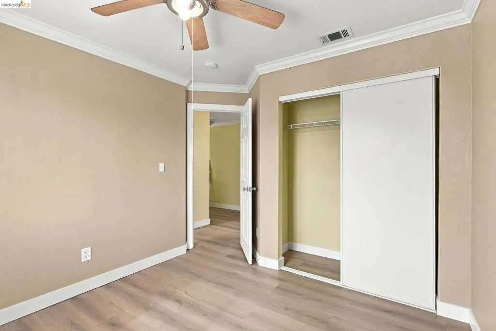 Interior space featuring wood-finish flooring, ceiling fan with light fixture, crown molding, and closet with sliding doors