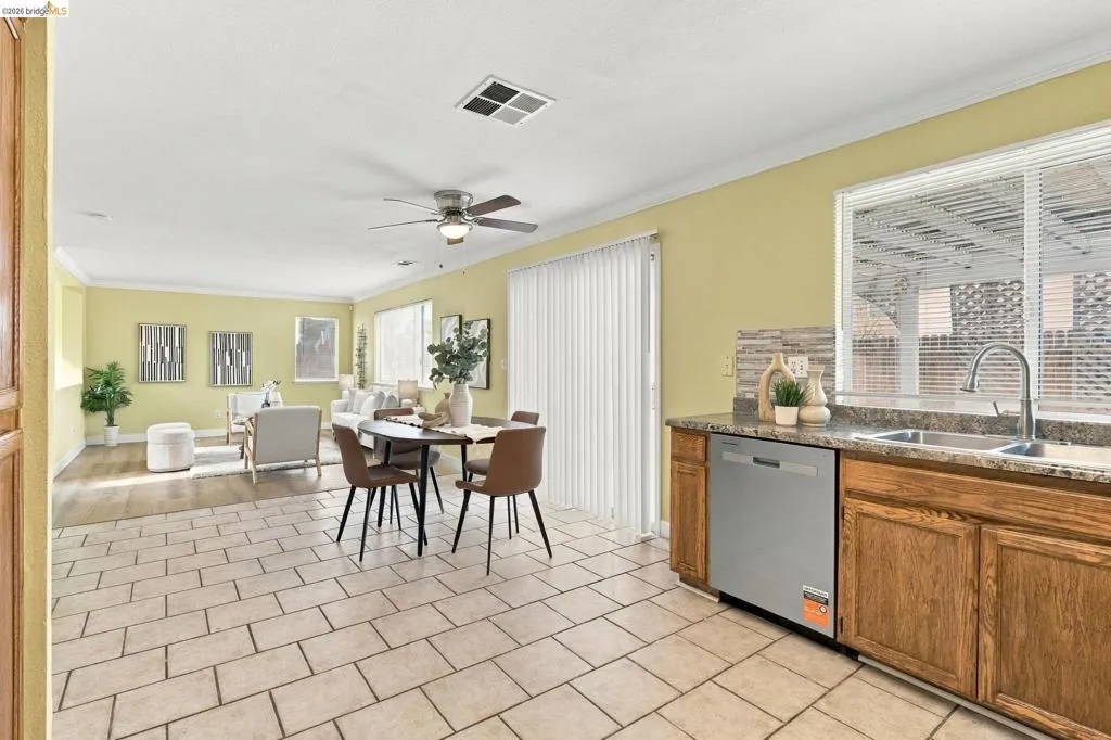 Kitchen featuring wood cabinetry, stone-finish countertops, stainless steel dishwasher, and tile flooring, complemented by sliding glass patio doors