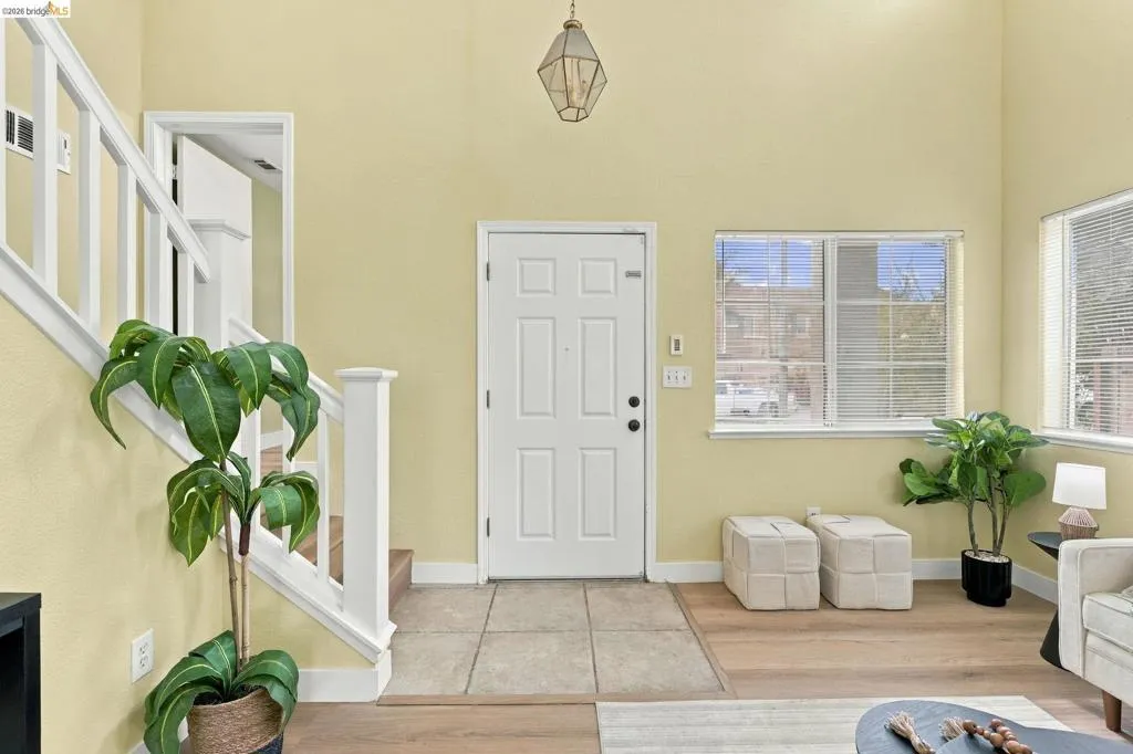 Foyer featuring high ceilings, wood-finish flooring, tiled entryway, white staircase railings, and geometric pendant lighting