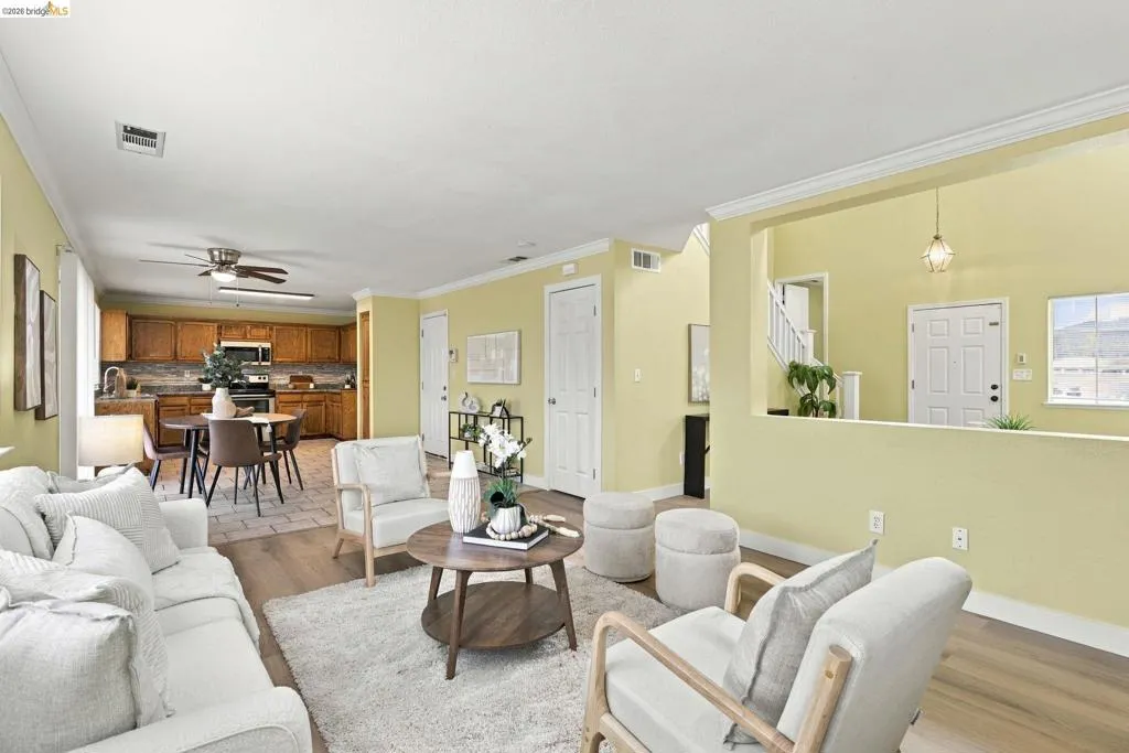 Open-concept area featuring wood-finish flooring, crown molding, a kitchen with wooden cabinetry, and a ceiling fan