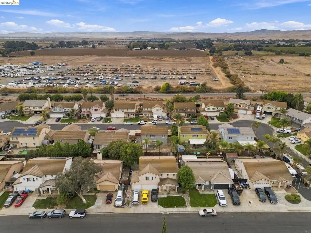 Aerial perspective of suburban residential neighborhood featuring multi-story homes with composition shingle roofs, integrated garages, solar panel installations, and landscaped front yards