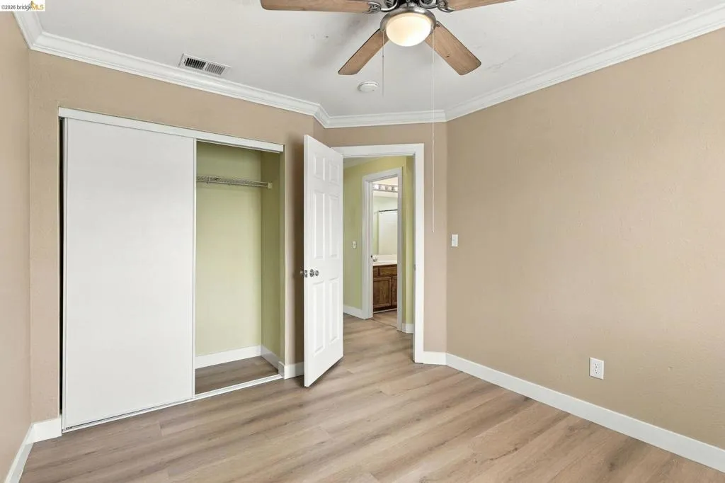 Wood-finish flooring, ceiling fan with integrated lighting, crown molding, and closet with sliding doors