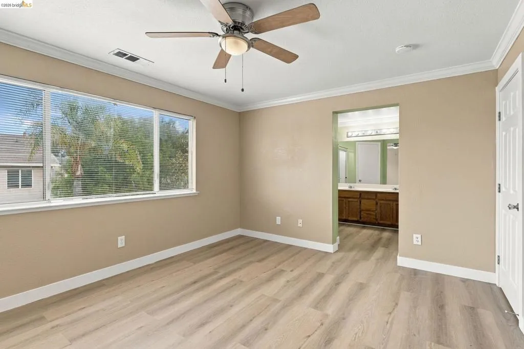 Room featuring wood-finish flooring, a multi-blade ceiling fan with integrated lighting, expansive window with horizontal blinds, and crown molding