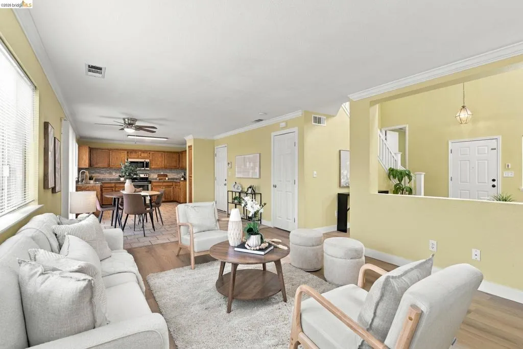 Open-concept interior featuring wood-finish flooring, crown molding, a kitchen with wooden cabinetry, and a ceiling-mounted light fixture