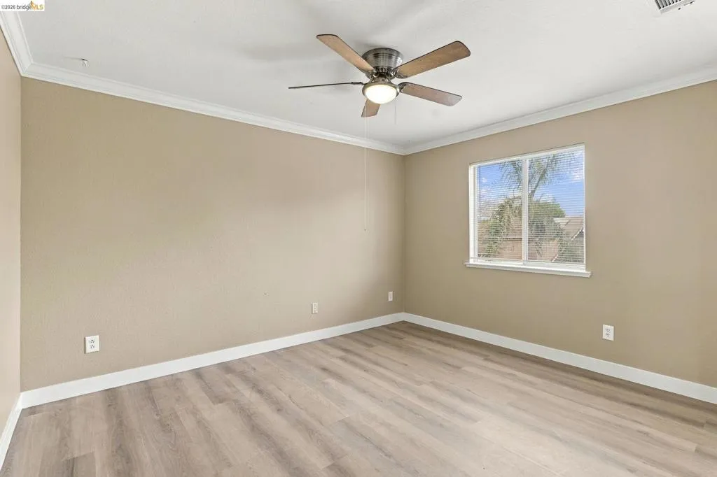 Neutral-toned interior featuring wood-finish flooring, crown molding, and a central ceiling fan with integrated lighting