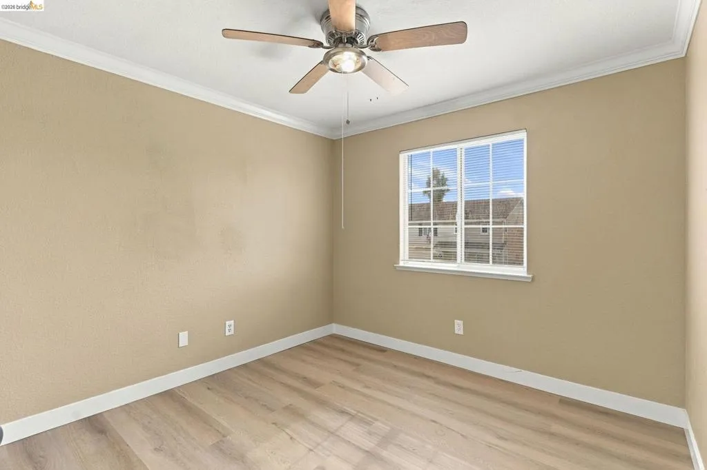 Room featuring wood-finish flooring, a multi-lite window, crown molding, and a ceiling fan with integrated lighting
