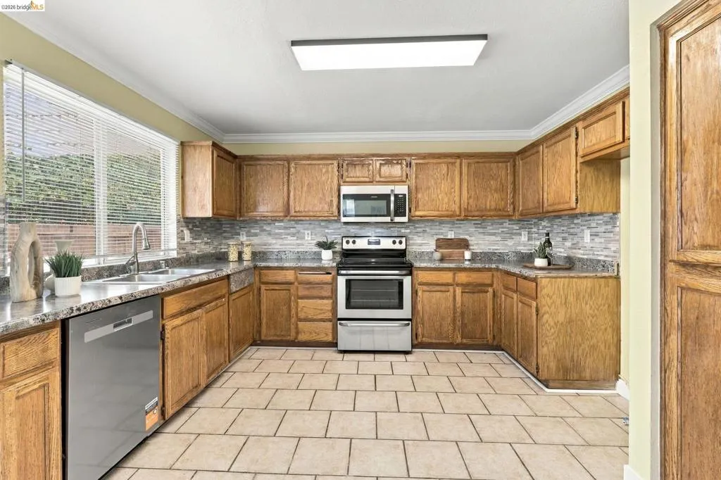 Kitchen featuring wood cabinetry, stone-finish countertops, tile backsplash, stainless steel appliances, and ceramic tile flooring