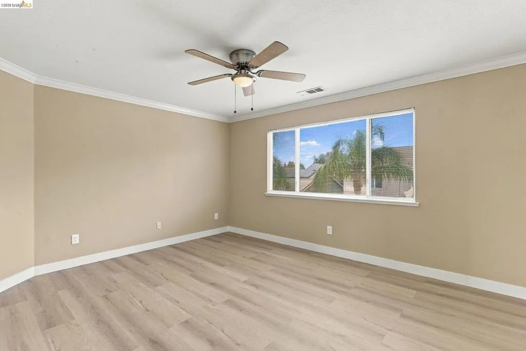 Room featuring wood-finish flooring, crown molding, a ceiling fan with integrated lighting, and a large window
