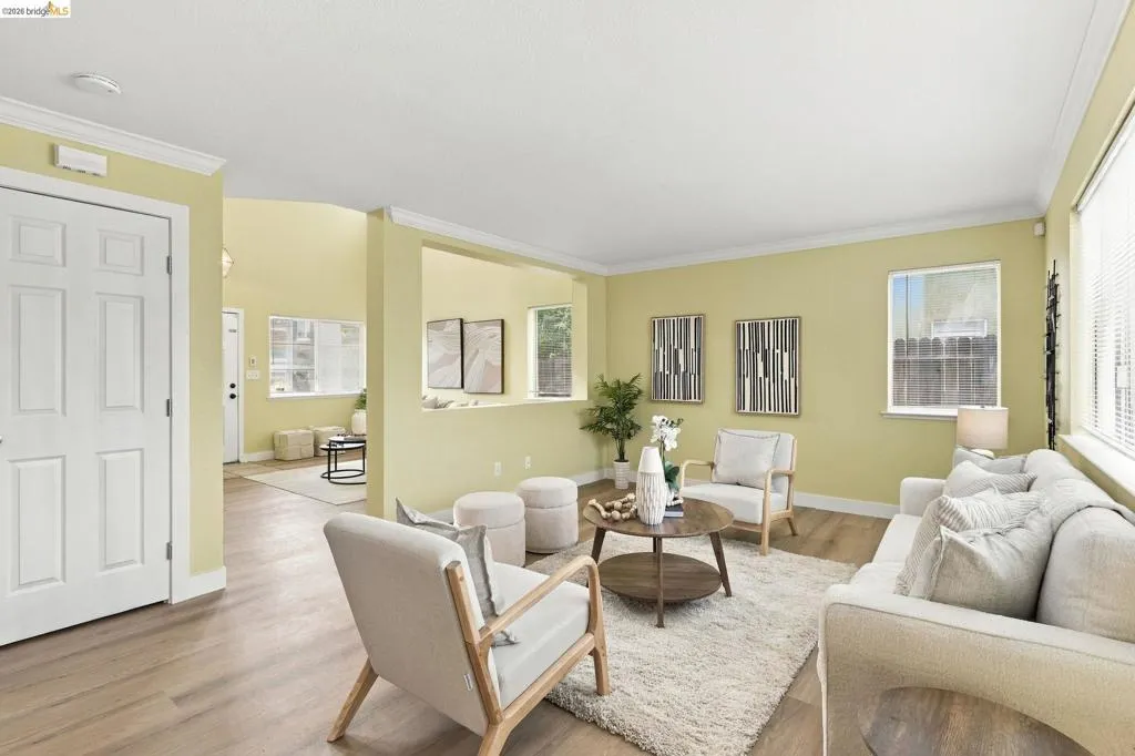 Open-concept interior featuring wood-finish flooring, multi-pane windows, crown molding, and a pass-through wall cutout