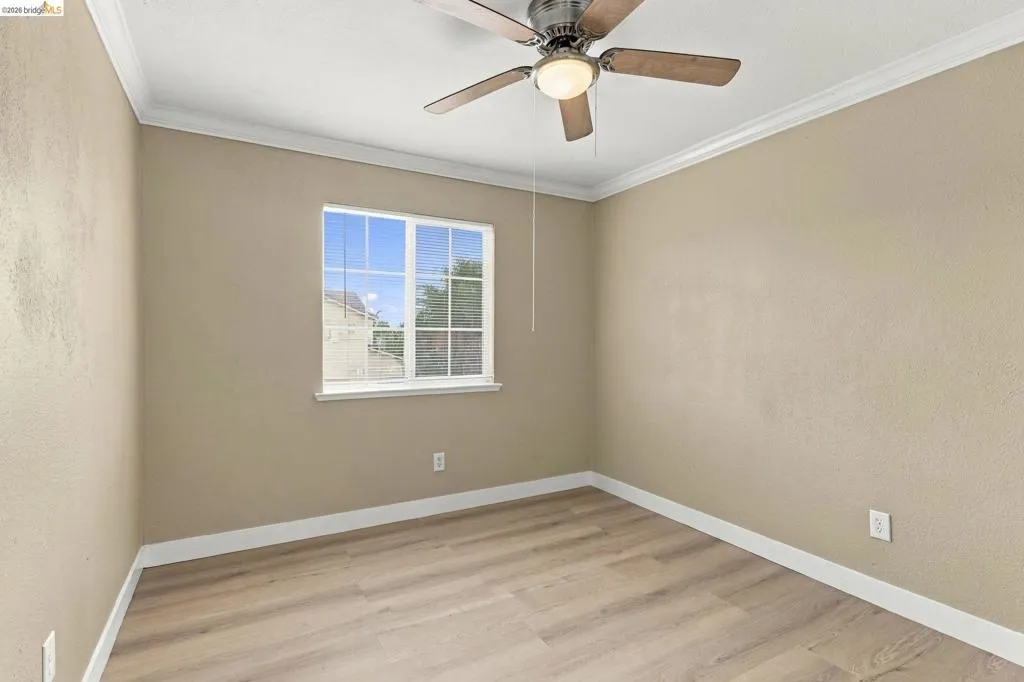 Neutral-toned room featuring wood-finish flooring, crown molding, a single-hung window with muntins, and a ceiling fan with integrated lighting