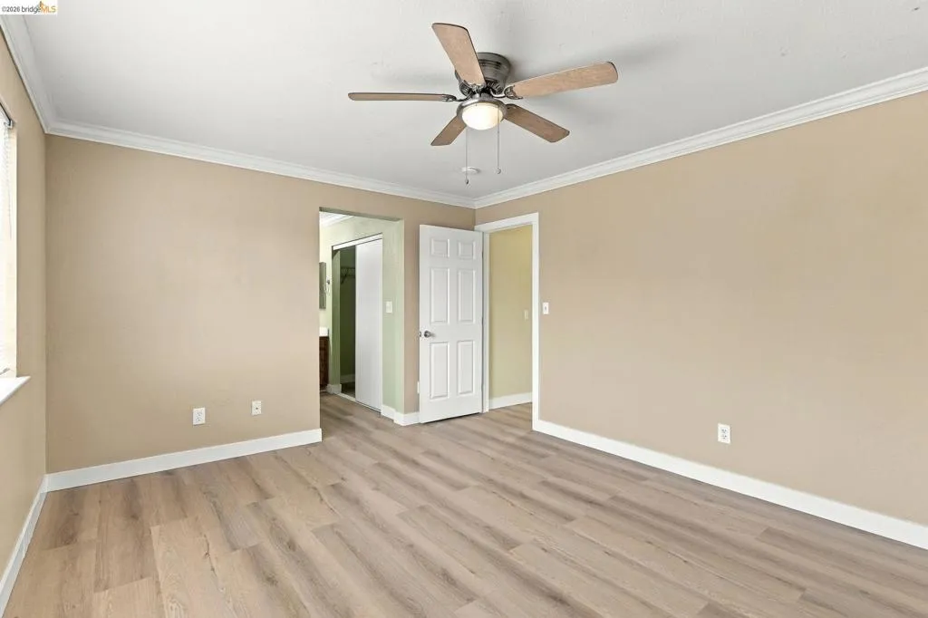 Room featuring wood-finish flooring, crown molding, and a central ceiling fan with integrated lighting