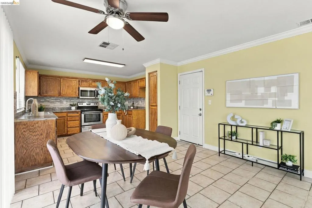 Kitchen featuring stained wood cabinetry, stone-tile backsplash, tile flooring, and a ceiling fan with integrated lighting
