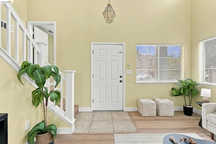 Foyer featuring high ceilings, wood-finish flooring, tiled entryway, white staircase railings, and geometric pendant lighting