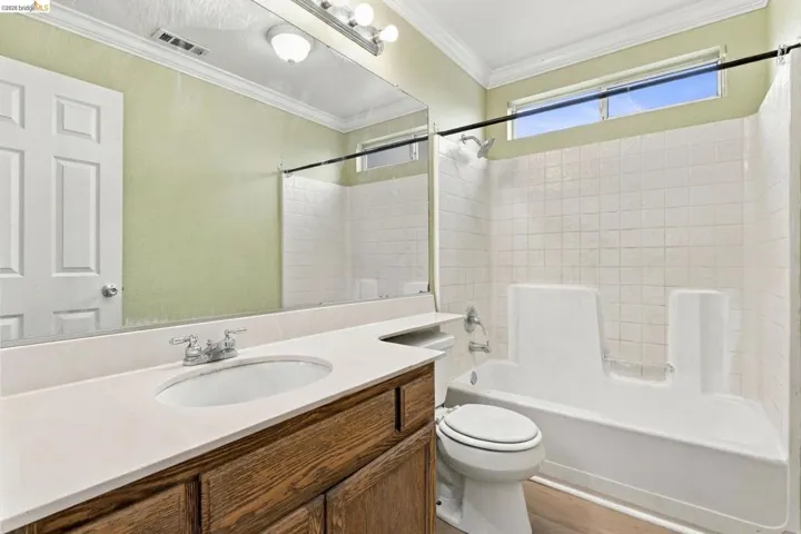 Bathroom featuring a wood-finish vanity with a solid-surface countertop, an integrated sink, a full-width mirror, and a bathtub with a tiled surround
