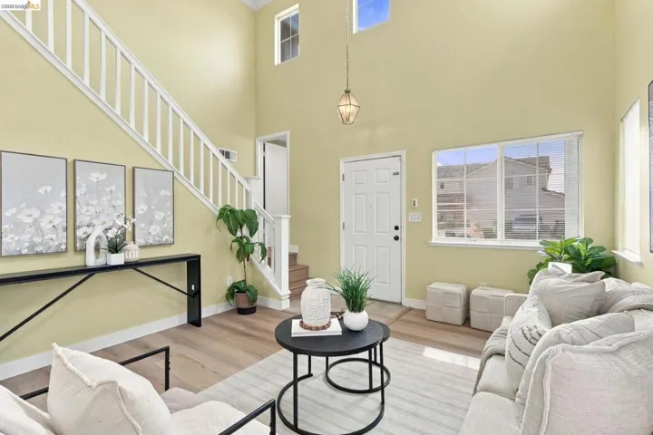 Two-story ceiling height featuring natural light, wood-finish flooring, staircase with white railing, and a multi-pane grid window