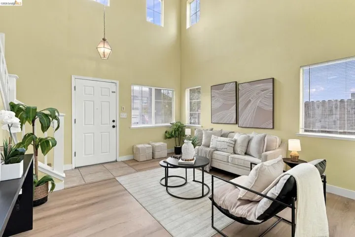 Double-height ceiling, wood-finish flooring, tiled entryway, multiple windows, and a tiered hanging pendant light