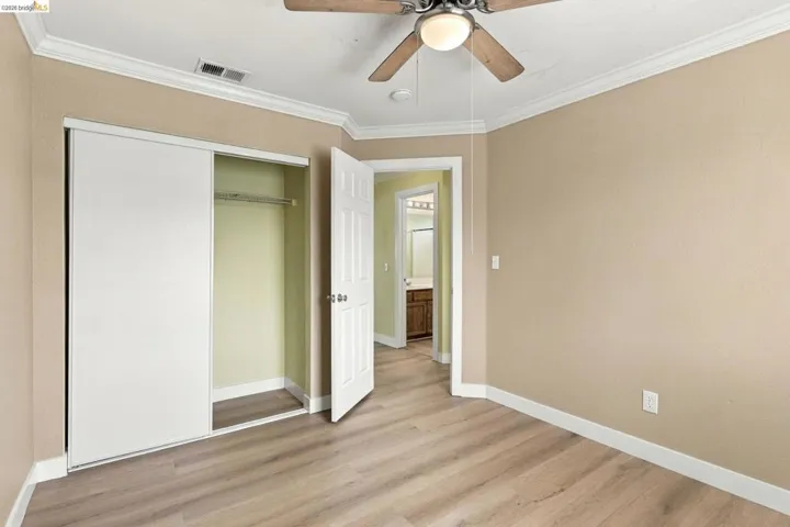 Wood-finish flooring, ceiling fan with integrated lighting, crown molding, and closet with sliding doors