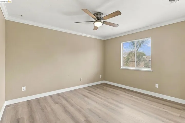 Neutral-toned interior featuring wood-finish flooring, crown molding, and a central ceiling fan with integrated lighting