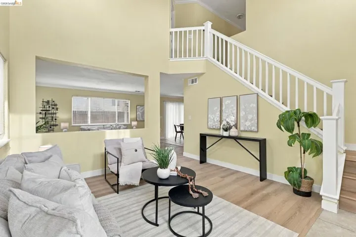Two-story ceiling height, staircase with white wooden balustrade, wood-finish flooring, and pass-through wall opening