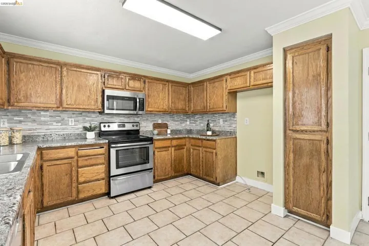Kitchen featuring wood cabinetry, stone-finish countertops, tile backsplash, stainless steel appliances, and tile flooring