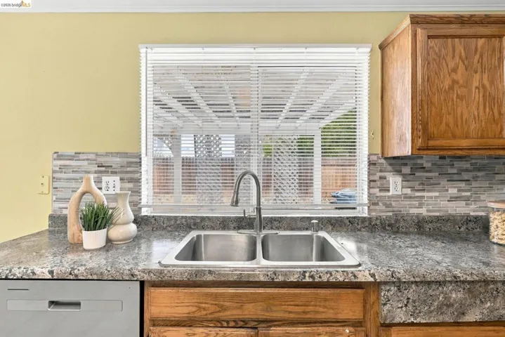 Stainless steel dual-basin undermount sink with arched pull-down faucet, multi-tonal linear tile backsplash, and stone-finish countertop