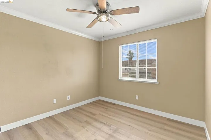 Room featuring wood-finish flooring, a multi-lite window, crown molding, and a ceiling fan with integrated lighting