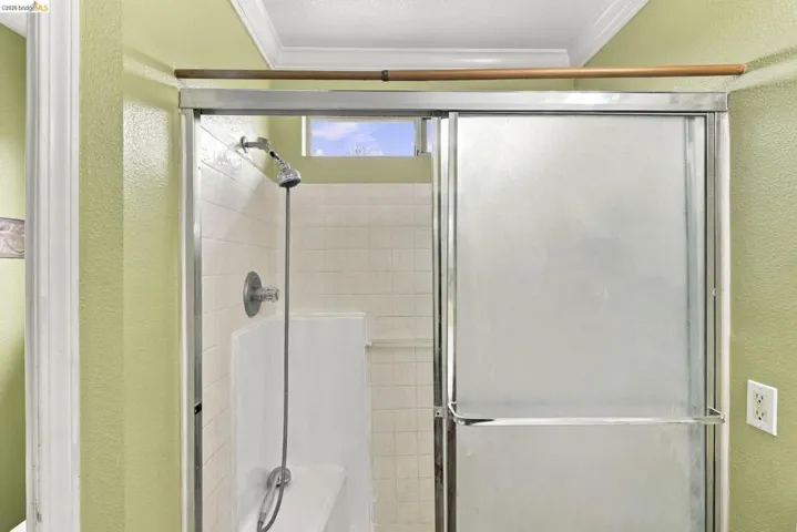 Shower enclosure featuring sliding frosted glass doors, chrome hardware, a handheld shower fixture, built-in bench seating, and light-toned tile surround