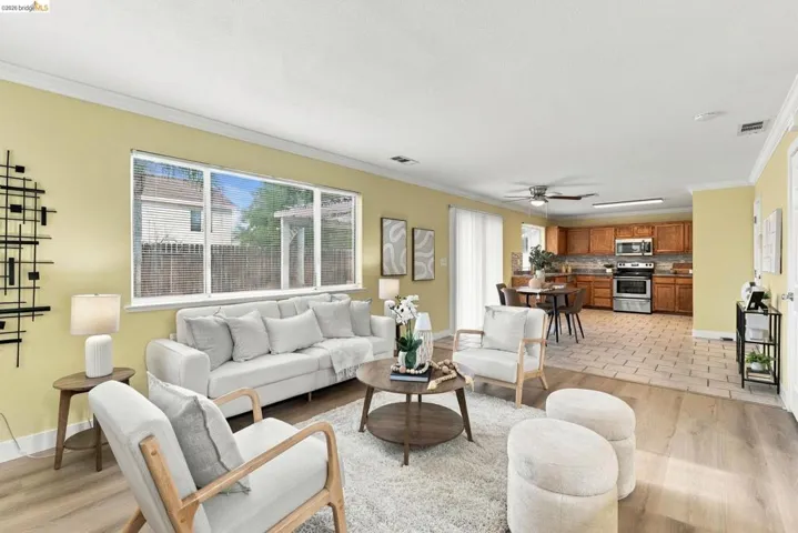 Open floor plan featuring wood-finish flooring, large picture window, crown molding, ceiling fan, and kitchen with wood cabinetry