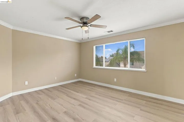 Room featuring wood-finish flooring, crown molding, a ceiling fan with integrated lighting, and a large window
