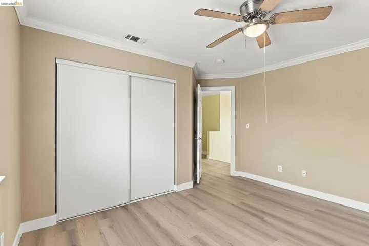 Room featuring wood-finish flooring, sliding-door closet, crown molding, and a ceiling fan with integrated lighting