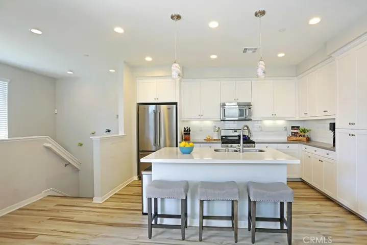 Large kitchen feels like a single family home with lots of cabinets, subway tile full backsplash, white quartz island and coordinating gray quartz countertops, stainless steel appliances including refrigerator and marble look pendants.