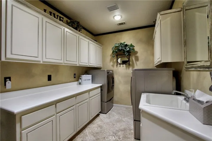 Laundry room with cabinets, counter and sink.  There are 2 dryers and one washer in the room currently.