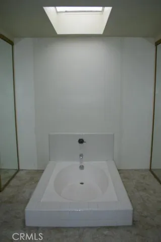 Sunken tub with skylight above and mirrored closet doors on both sides of the tub
