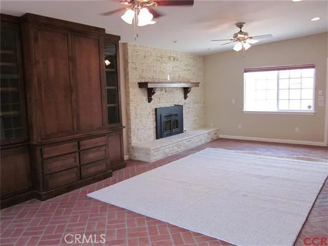 Family room with stone brick fireplace, built in entertainment cabinet and brick floor.