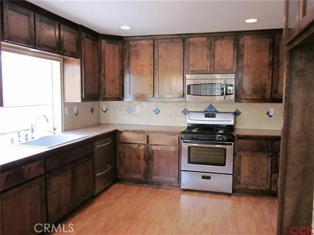 Kitchen features stainless appliances, dark wood cabinetry, tile backsplash and wood floor. Very attractive.