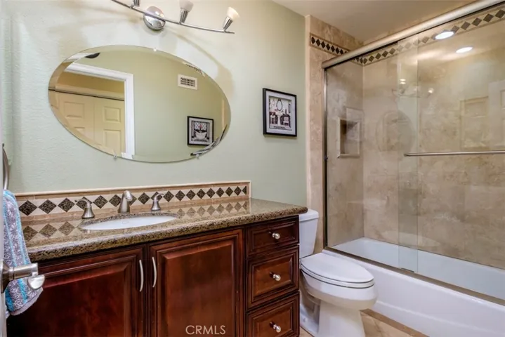 Remodeled guest bath with newer vanity, granite counter top, new toilet, and shower/tub combo with travertine wall, shampoo niche and glass enclosure.
