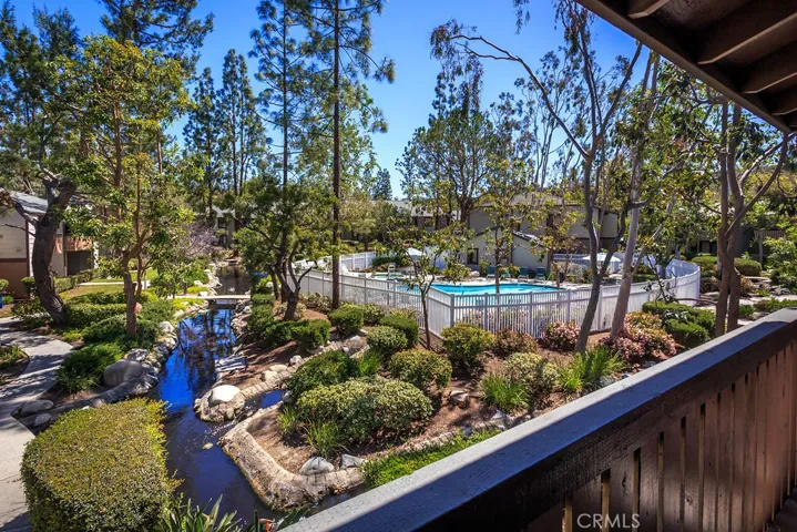 View from the balcony deck.  Foreground features running stream with lush vegetation and full grown trees.  Background includes one of the three pool and spa area.