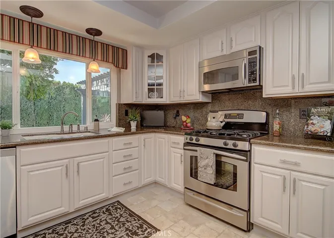 Gleaming kitchen with granite counters travertine floors and stainless accents...lovely view of rear yard too!