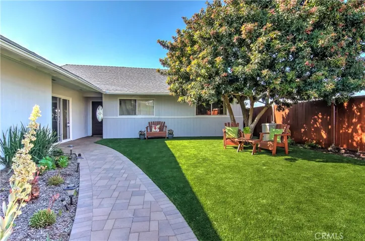 Private front courtyard, with artificial turf, concrete paver walkway, mature and full tree, and garden border along the fence.