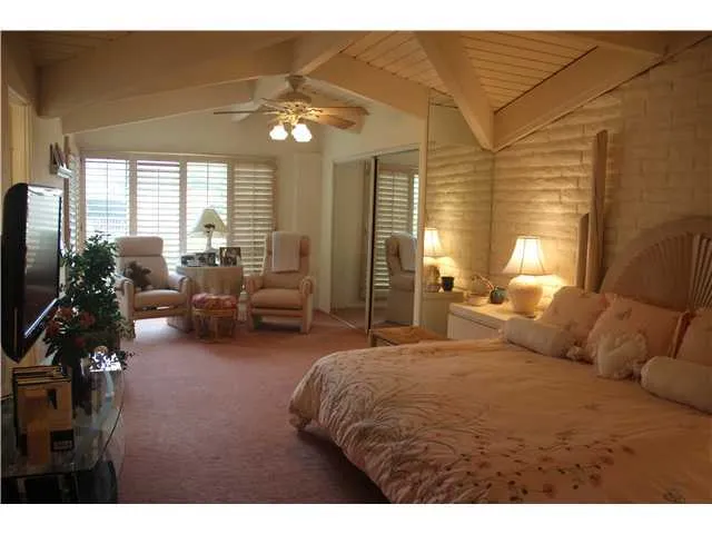 Master bedroom with vaulted ceilings, sitting area, plantation shutters, mirrored wardrobe closets and ceiling fan,