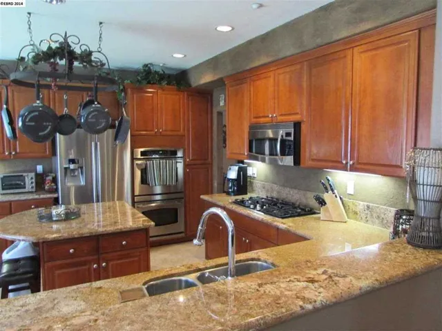 Shows double oven, under-cabinet lighting, pot rack, stainless steel appliances and island